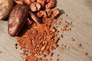 Cocoa beans next to powdered cocoa on a wooden surface