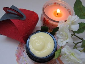 Organic cream next to a candle, white flowers and a red packaging